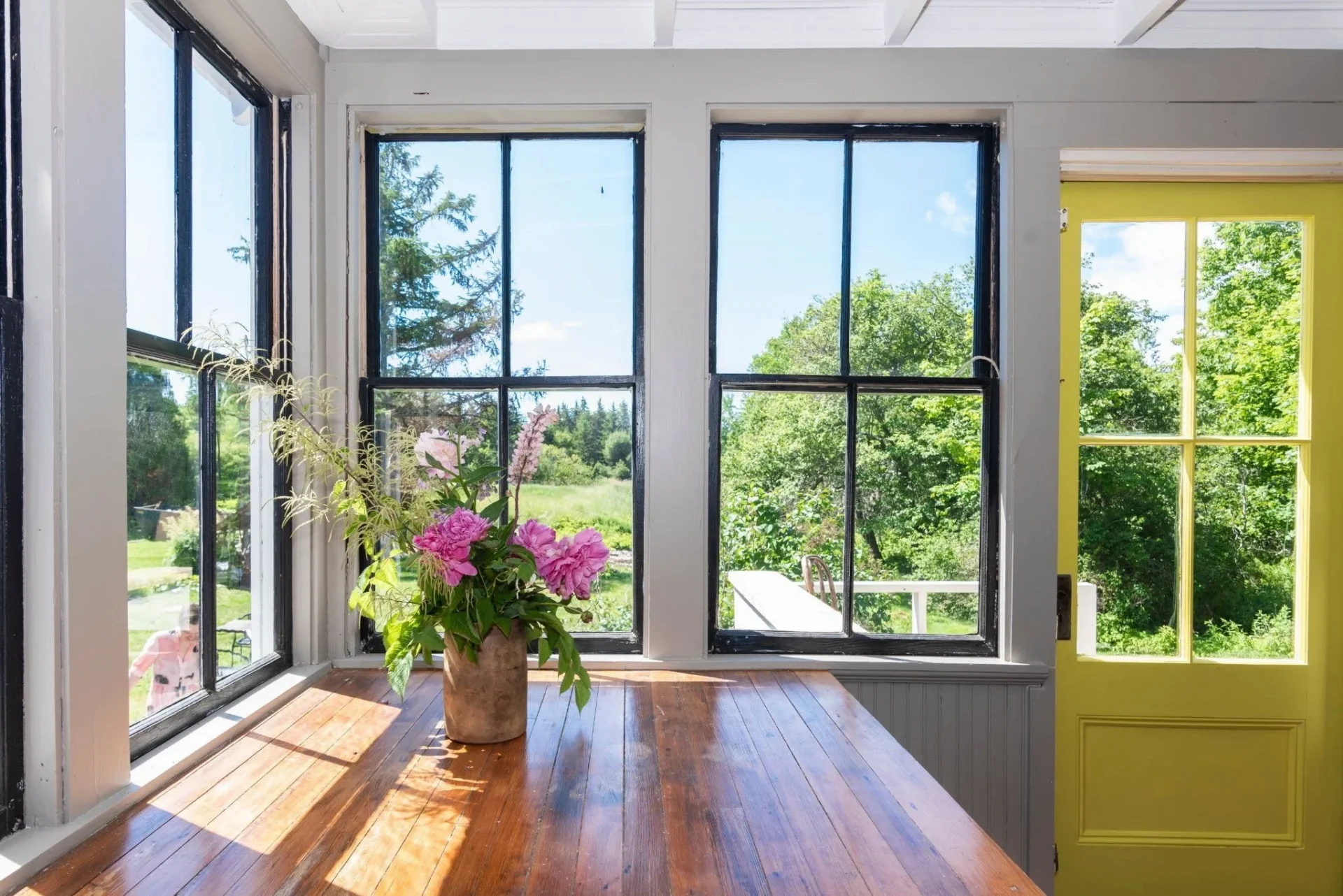 beautiful windows and lighting on a wood table with some nice flowers in a vase.